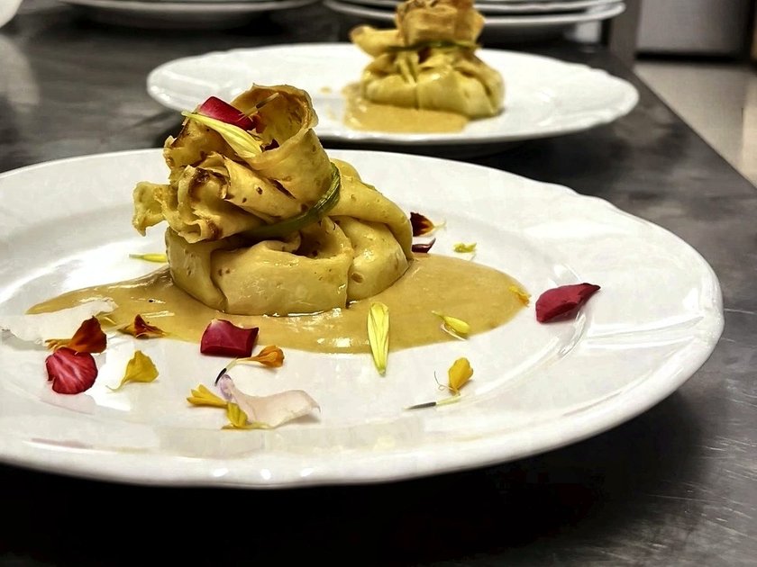 Un fagottino di crespella con la salsa e i petali di fiore